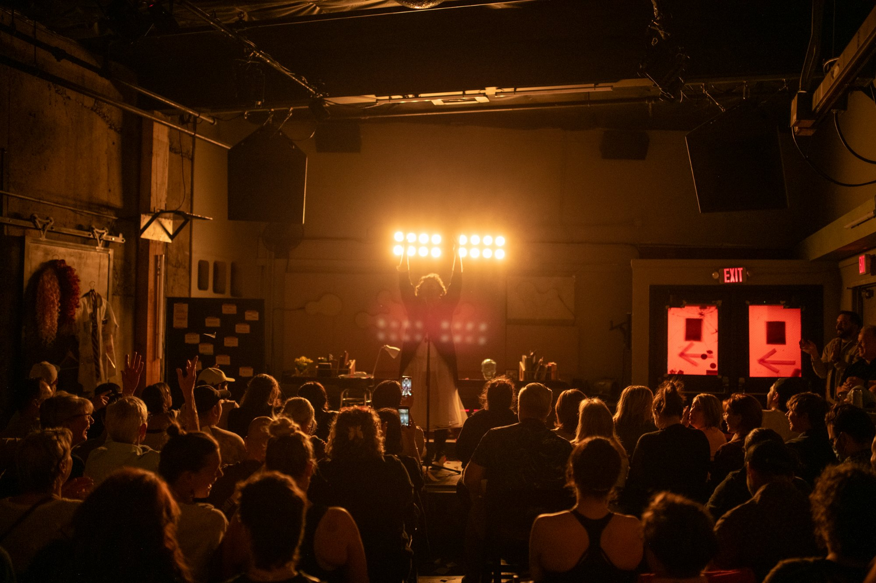 Bottoming for Jesus — Michael with arms raised, audience seen from behind, warm golden stage light